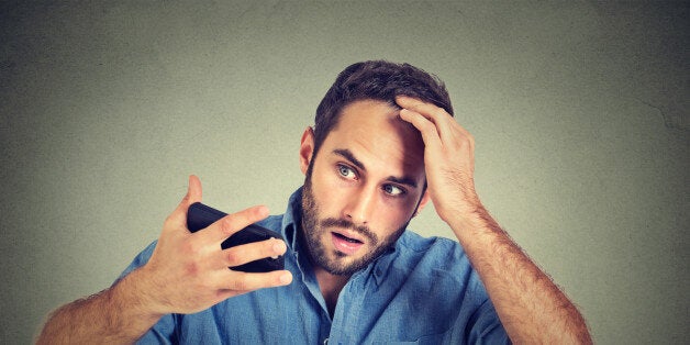 Closeup portrait, shocked man feeling head, surprised he is losing hair, receding hairline, bad news isolated on gray wall background. Negative facial expressions, emotion feeling