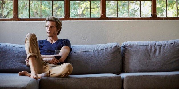 Mid adult man holding red wineglass while sitting on sofa at home