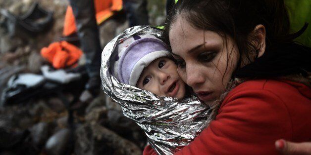 A woman hugs a baby wrapped in an emergency blanket as refugees and migrants arrive on the Greek island of Lesbos after crossing the Aegean sea from Turkey on October 1, 2015. (Photo credit should read ARIS MESSINIS/AFP/Getty Images)