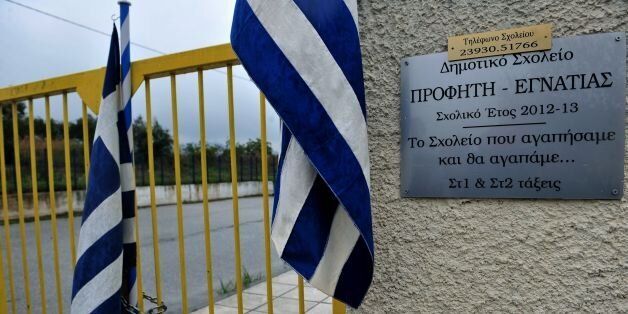 Greek flags are attached to the gate of a school after residents locked it to protest against the schooling of refugee children, on October 10, 2016 in Profitis, a village 40km east of Thessaloniki. Greece began schooling some 1,500 children of refugees stuck in the country on October 10, starting in 20 schools in greater Athens, Thessaloniki and other parts of the country, and a gradual operation of other areas following the progress of the vaccination drive, said the Education ministry general secretary. Last month parents in Oreokastro, a district near Thessaloniki, said they would not allow refugee children in their schools for health reasons, a stance condemned by the government. The plaque reads 'The school that loved and we love'. / AFP / Sakis Mitrolidis (Photo credit should read SAKIS MITROLIDIS/AFP/Getty Images)
