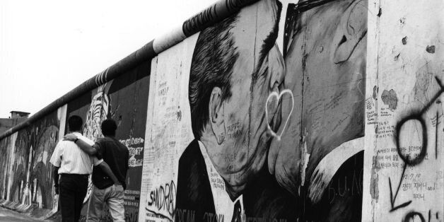 A gay couple strolling past graffiti on the Berlin Wall depicting German leaders Leonid Brezhnev and Erich Honecker sharing a kiss, August 1993. (Photo by Steve Eason/Hulton Archive/Getty Images)