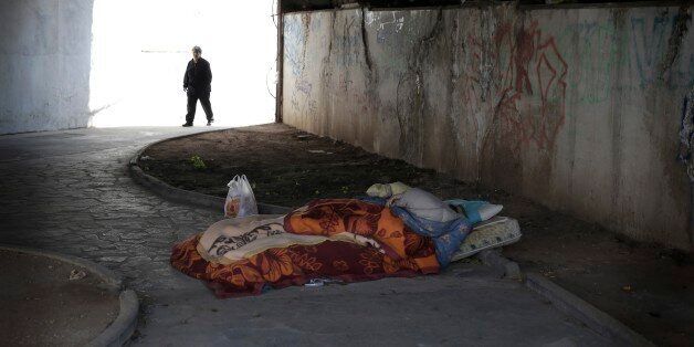 A homeless man sleeps under a bridge as an elderly woman walks past in Athens, Thursday March 19, 2015. Parliament on Wednesday approve an anti-poverty bill, that would provide assistance worth some 200 million euros ($212.7 million) to mostly jobless households considered to be in