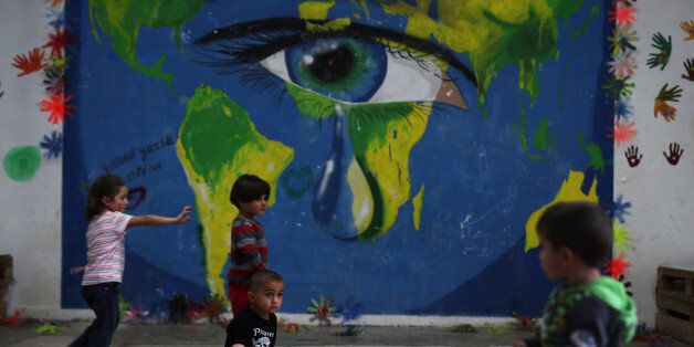 In this photo taken on Tuesday, Sept. 13, 2016, children play in front of a mural at Ritsona refugee camp north of Athens. Most of the people at the camp arrived in Greece in March, crossing to Lesbos and Chios just ahead of an agreement between the EU and Turkey that took effect. Under the deal, anyone arriving on Greek islands from Turkey on or after March 20 would be held on the island and face being returned to Turkey. Balkan countries began restricting crossings of their borders in early 20