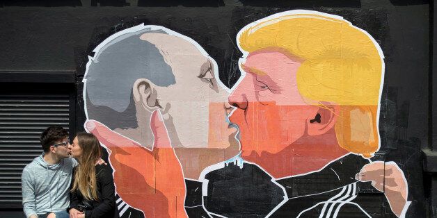 A couple kisses in front of graffiti depicting Russian President Vladimir Putin, left, and Republican presidential candidate Donald Trump, on the walls of a bar in the old town in Vilnius, Lithuania, Saturday, May 14, 2016. (AP Photo/Mindaugas Kulbis)