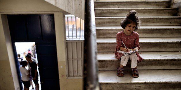 A young girl drawsas she sits in the stairs of an abandoned school used by volunteers for hosting Syrian and Afghan refugees in Athens on July 1, 2016.Some 250 people live in self-management in the school of Athens city center, closed for three years. The families occupy three floors of the building, and twenty classrooms, where a tense sheets forest delineate areas of life and protect privacy. The squat was established in mid-March, when the sudden closure of their borders with the countries north of Greece makes it a trap for those who relied only cross to reach Germany or Sweden. Almost all e now living in dozens of camps set up in haste by the government. Some rent rooms. The others are squat. The government estimates about 1,500 the number of people living well into 'outdoor hospitality structures.' / AFP / ARIS MESSINIS (Photo credit should read ARIS MESSINIS/AFP/Getty Images)