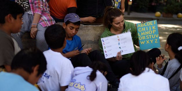 A volunteer teaches refugee children reading and writing in Victoria Square, Athens on April 27, 2016. Victoria Square is an unofficial place where refugees gather in Athens. (Photo by Gili Yaari/NurPhoto via Getty Images).