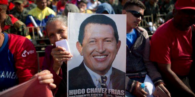 A woman holds a poster of the late President Hugo Chavez during a ceremony marking the third anniversary of his death, in an outdoor patio of the 4F military museum in Caracas, Venezuela, Saturday, March 5, 2016. Chavez died of cancer at age 58 on March 5, 2013. (AP Photo/Ariana Cubillos)