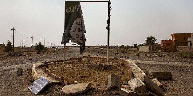 In this Sunday, August 28, 2016 photo, a partially destroyed Islamic State group banner hangs at the entrance to Qayara, Iraq. The skies above Qayara are black with the smoke from more than a dozen oil wells set alight by Islamic State group fighters attempting to obstruct airstrikes as Iraqi forces pushed into the the town on bank of the Tigris last week and took control of the entire area Thursday. (AP Photo/Susannah George)