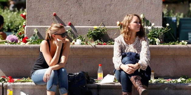 Two women rest at the base of a monument decorated with flowers in respect of the victims in last Friday's killing spree and bomb attack in Oslo, July 27, 2011. Norwegians tried to restore some normality on Wednesday after mass killings by a far-right zealot traumatised the nation, but a security alert forced the evacuation of Oslo station. REUTERS/Cathal McNaughton (NORWAY - Tags: CIVIL UNREST CRIME LAW SOCIETY)