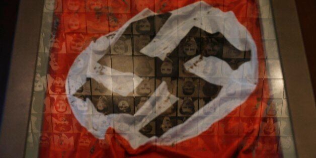 In this photo taken Saturday, March 21, 2015, a Nazi flag is displayed at the Holocaust Museum in the town of Kalavryta, western Greece, as portraits of victims are reflected in a glass pane. It was 1943 and the Nazis were deporting Greece's Jews to death camps in Poland. Hitler's genocidal accountants reserved a chilling twist: The Jews had to pay their train fare. The bill for 58,585 Jews sent to Auschwitz and other camps exceeded 2 million Reichsmark â more than 25 million euros ($27 million) in today's money. For decades, this was a forgotten footnote among all of the greater horrors of the Holocaust. Today it is returning to the fore amid the increasingly bitter row between Athens and Berlin over the Greek financial bailout. (AP Photo/Petros Giannakouris)