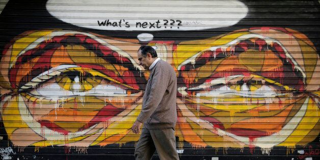 In this photo made on Tuesday, April 29, 2015, a Greek man walks past a graffiti in central Athens. Wednesday May 6 marks five years since Greece voted in its first bailout deal in the face of violent popular protests that left three dead. The day was followed by years of turmoil in which the country tried to overhaul its economy in the midst of a downturn matched in depth and length only by the Great Depression. (AP Photo/Petros Giannakouris)