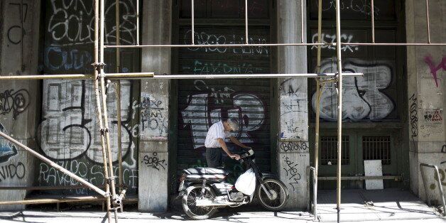 A man leans over the handlebars of his bike in front of a graffiti-sprayed wall on a street in downtown Athens, Greece, August 25, 2015. Greece's radical left Syriza party can win re-election with an outright majority, a senior member said on Tuesday, governing without support from mainstream forces which also back the country's new international bailout. REUTERS/Stoyan Nenov