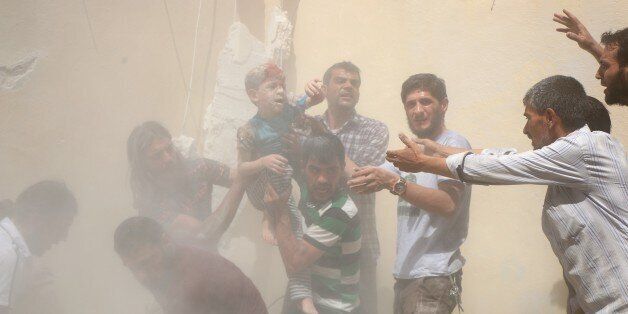 ALEPPO, SYRIA - JULY 17: (EDITOR'S NOTE: Image contains graphic content.) A Syrian man carries a wounded boy in his arms after the war-craft belonging to the Russian army bombed the opposition controlled residential area at the Al-Maysir neighborhood in Aleppo, Syria on July 17, 2016. (Photo by Beha el Halebi/Anadolu Agency/Getty Images)