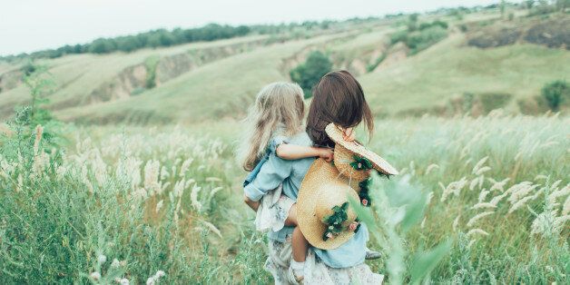 The back view of young mother and daughter on green grass background.