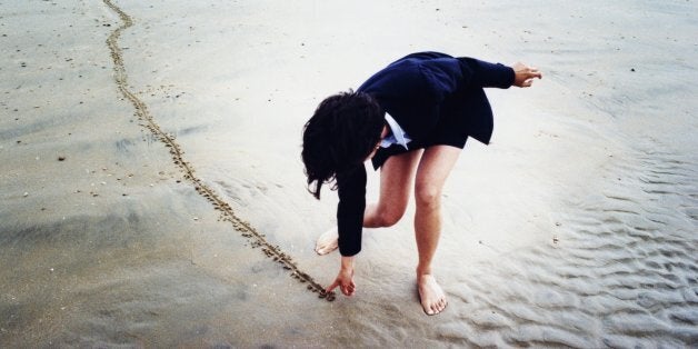 Young businesswoman drawing line in sand on beach