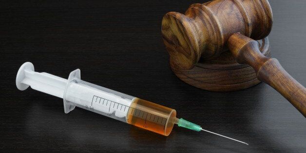 Judges Gavel And Medical Injection Syringe With Brown Liquid On The Black Wood Background, Close-up, Top View