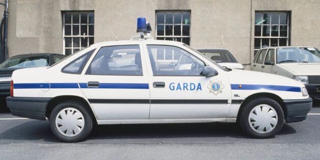 Republic of Ireland, Garda patrol car parked in front of civilian cars, outside grey building, side view.