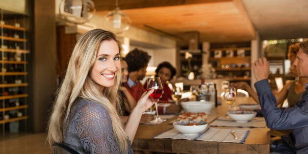 Smiling woman holding a glass at a table having dinner with friends.
