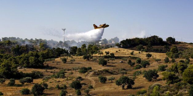 A firefighting plane drops water over a fire near holiday homes in Costa village in the Argolida region, in Southeastern Greece during a developing wild fire, July 20, 2015. Dozens of people were evacuated as firefighters fought the fire, which broke out on Monday afternoon in Panorama in Costa village at a forested area where dozens of summer houses are located, according to local media. REUTERS/Yannis Behrakis