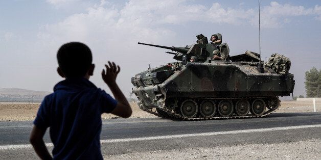 A child waves toward Turkish troops heading to the Syrian border, in Karkamis, Turkey, Friday, Aug. 26, 2016. Turkey's state-run Anadolu news agency said late Thursday Turkish artillery have shelled a group of Syrian Kurdish militia fighters in the north of the town of Mambij after they allegedly ignored warnings to retreat. (AP Photo/Halit Onur Sandal)