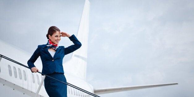 'Outdoor portrait of a beautiful flight attendant standing on the aircraft stairs, waiting for travellers.'