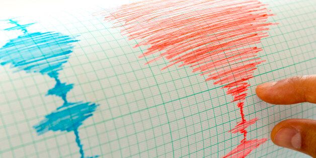 Seismological device for measuring earthquakes. Seismological activity live on the sheet of measuring paper. Earthquake wave on graph paper. Human hand showing earthquake.
