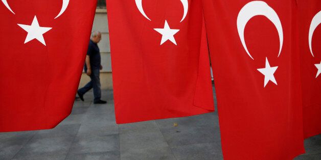 A man walks along a street behind some Turkish flags in Istanbul, on Saturday, July 30, 2016. Turkey has demanded the United States extradite Fethullah Gulen, a cleric living in self-imposed exile in Pennsylvania whom it accuses of being behind the violent July 15 coup attempt that left more than 200 people dead. (AP Photo/Petros Karadjias)