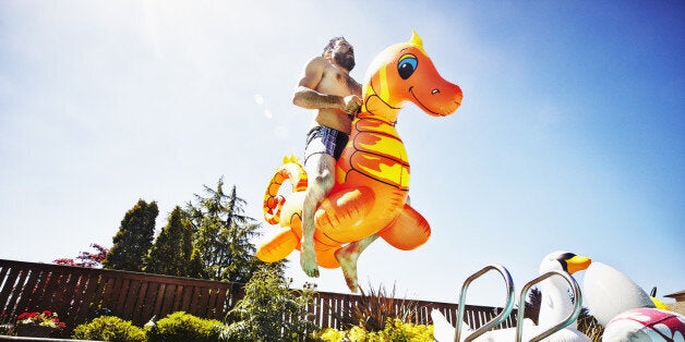 Man jumping into outdoor pool with inflatable pool toy on summer afternoon