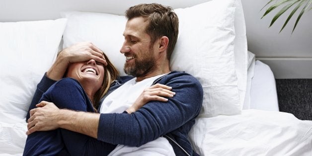 Young woman lying on mattress with man covering eyes of his girlfriend - Indoors