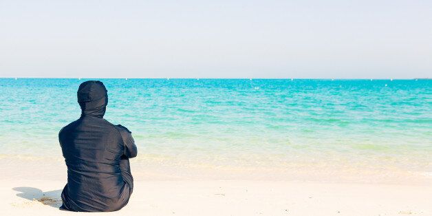 young woman wearing burkini sitting by the beach in dubai