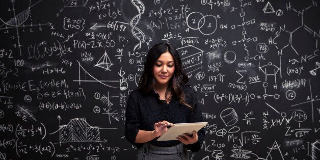 A young woman stands using her tablet in front of a chalkboard filled with mathematical equations, showing individuality, intelligence and creativity