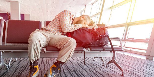 Man sleeping on his travel luggage inside airport terminal with back light bright sun coming throw window