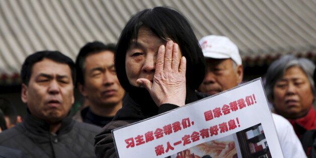 Dai Shuqin, whose family members were onboard Malaysia Airlines flight MH370 which went missing in 2014, wipes away tears as she holds a placard with Chairman Xi's photo on it, in front of a holding area for journalists at Lama Temple in Beijing, China, March 8, 2016. The Chinese characters on the placard reads