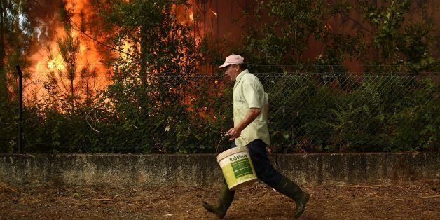 A villager runs with a bucket to takle a wildfire in Soutelo near Macinhata do Vouga, central Portugal, on August 9 2016.More than 3,000 people have been battling to contain roughly 100 fires across the country with 12 major blazes leading to the evacuation of local residents overnight. / AFP / FRANCISCO LEONG (Photo credit should read FRANCISCO LEONG/AFP/Getty Images)