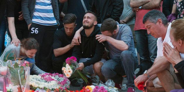 People mourn behind flower tributes near the Olympia shopping center where a shooting took place leaving nine people dead the day before, in Munich, Germany, Saturday, July 23, 2016. Police piecing together a profile of the gunman whose rampage at a Munich mall Friday left nine people dead described him Saturday as a lone, depression-plagued teenager. (AP Photo/Jens Meyer)