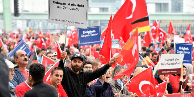 A Turkish protestor holds a banner reading 'Erdogan is a hero of democracy', left, during a demonstration in Cologne, Germany, Sunday, July 31, 2016. Supporters of Turkish President Recep Tayyip Erdogan demonstrate in Cologne amid heavy police presence. Some 30,000 participants are expected at Sunday's demonstration, which comes amid tensions following the failed coup attempt in Turkey and concern in Germany over the extent of the Turkish government's subsequent crackdown. (AP Photo/Martin Meissner)