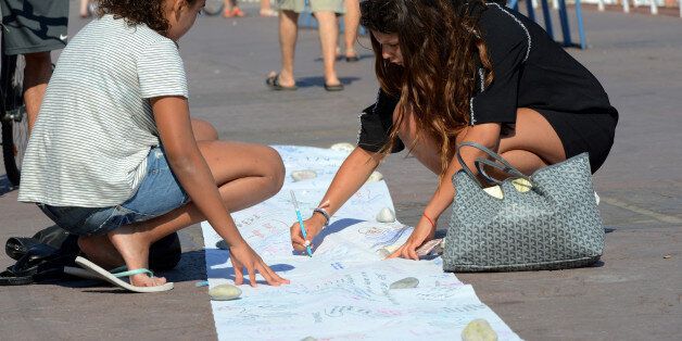 A woman writes a message on a long sheet of paper on the third day of national mourning to pay tribute to victims of the truck attack along the Promenade des Anglais on Bastille Day in Nice, France, July 18, 2016. REUTERS/Jean-Pierre Amet