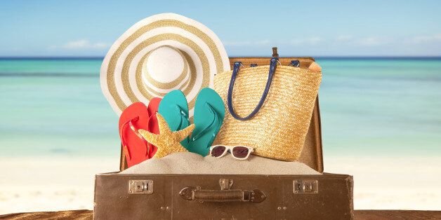 Travel concept with old suitcase on wooden planks full of beach accessories. Placed on mole with sandy beach on background