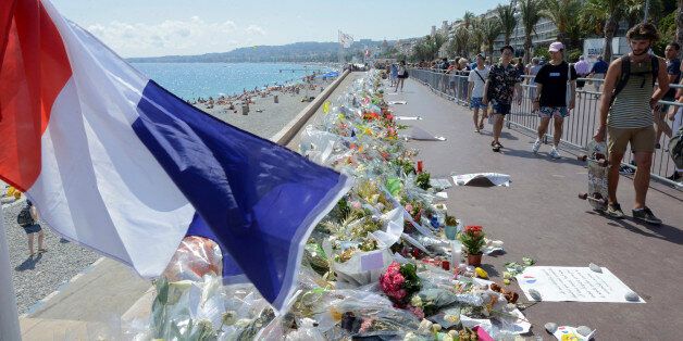 People walk past flowers left in tribute at a makeshift memorial to the victims of the Bastille Day truck attack near the Promenade des Anglais in Nice, France, July 21, 2016. REUTERS/Jean-Pierre Amet