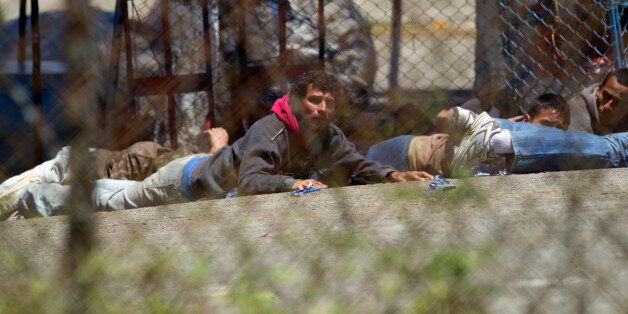 Seen through several chain link fences, people take cover after a riot broke out inside the Pavon prison in Guatemala City, Guatemala, Monday, July 18, 2016. Authorities in Guatemala say Byron Lima, an army captain serving a prison sentence for killing a Catholic bishop, has died during the riot. (AP Photo/Moses Castillo)