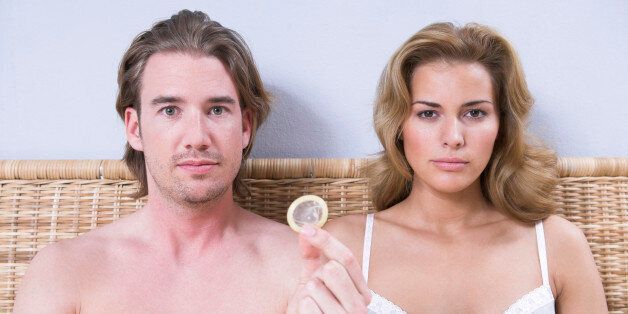 portrait of young couple sitting in bed man holding condom