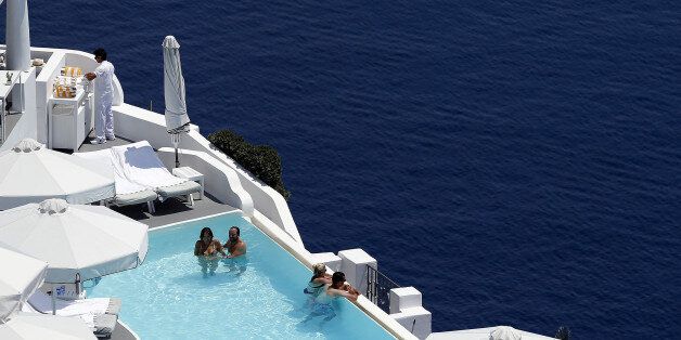Tourists relax in a private swimming pool in the village of Oia on the Greek island of Santorini, Greece, July 1, 2015. REUTERS/Cathal McNaughton/Files