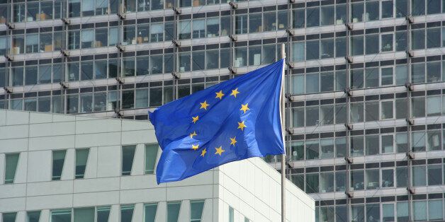 european union flag blowing in wind infront of office buildings