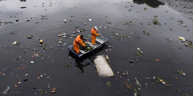 Men work cleaning up the garbage next to an ecobarrier at Meriti River which flows into Guanabara Bay, in Duque de Caxias, near Rio de Janeiro, Brazil, July 20, 2016. REUTERS/Ricardo Moraes