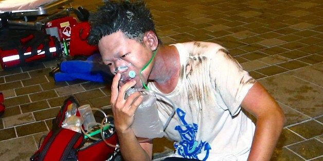 An injured man sits on the ground outside a station after an explosion on a passenger train in Taipei, Taiwan, Thursday, July 7, 2016. Taiwan's official news agency said an explosion that engulfed a commuter train car in flames has injured a number of people, some of them seriously. (AP Photo/Jerry Chen)