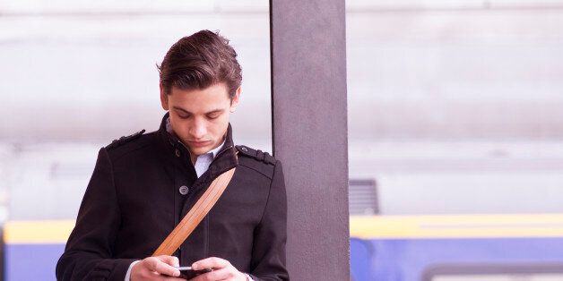 Man on train platform checks cell phone