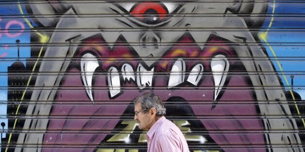 A man walks past graffiti painted on a closed shop at Monastiraki area in central Athens, Greece, July 7, 2015. Greece faces a last chance to stay in the euro zone on Tuesday when Prime Minister Alexis Tsipras puts proposals to an emergency euro zone summit after Greek voters resoundingly rejected the austerity terms of a defunct bailout. REUTERS/Christian Hartmann
