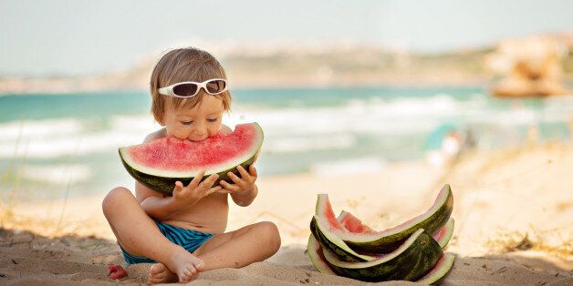 Boy eating piece of watermelon on the beach.