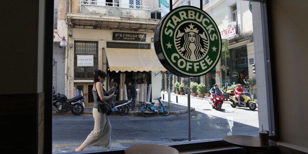 A pedestrian and scooter riders pass the window of a Starbucks Corp. coffee shop in Athens, Greece, on...