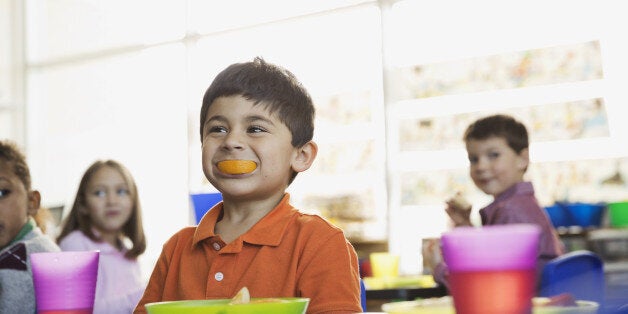 Playful boy holding orange slice in mouth at school at snack time